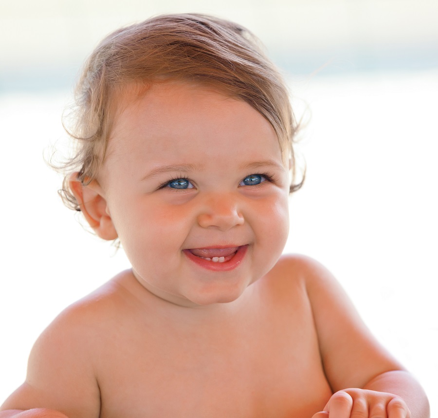 Portrait at the beach of a smiling one year old baby girl with blue eyes